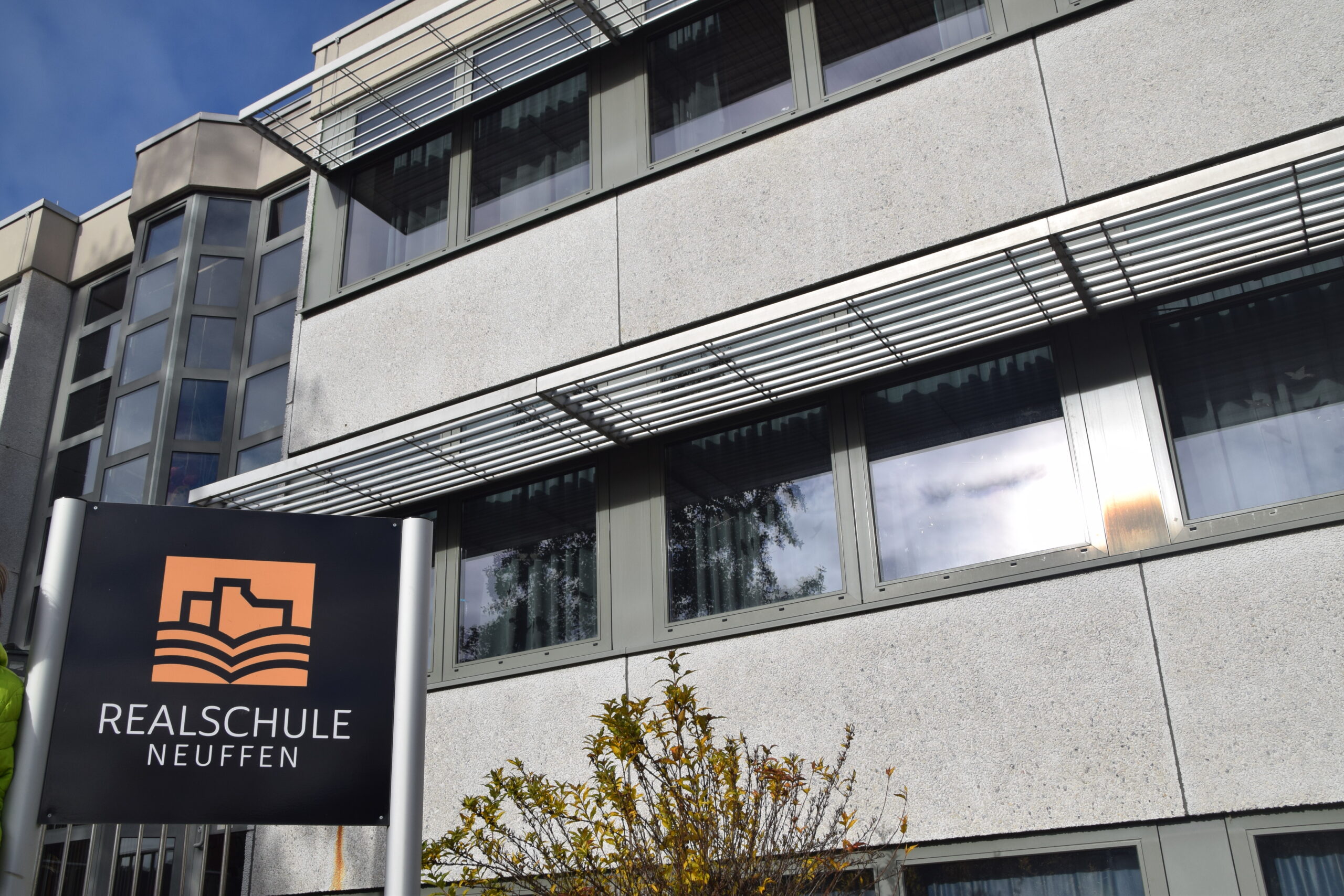 Schild mit dem Logo der Realschule Neuffen vor dem Schulgebäude