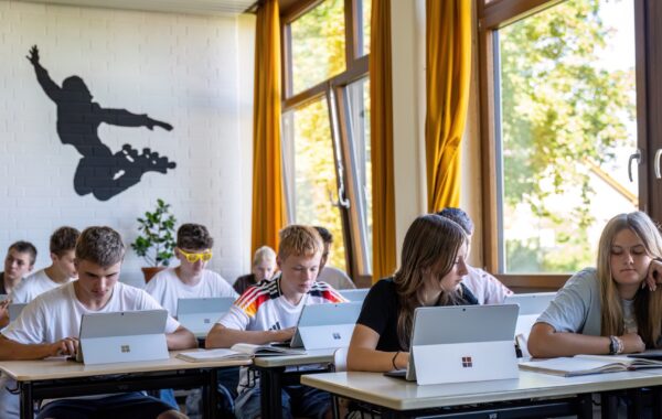 Schülerinnen und Schüler sitzen an Tischen im Klassenzimmer und arbeiten an Tabletts